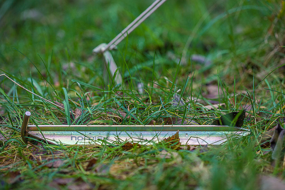 Nordisk Steel T-PEG Zelthering (2er-Set), einer im Gras eingeschlagen, einer daneben liegend