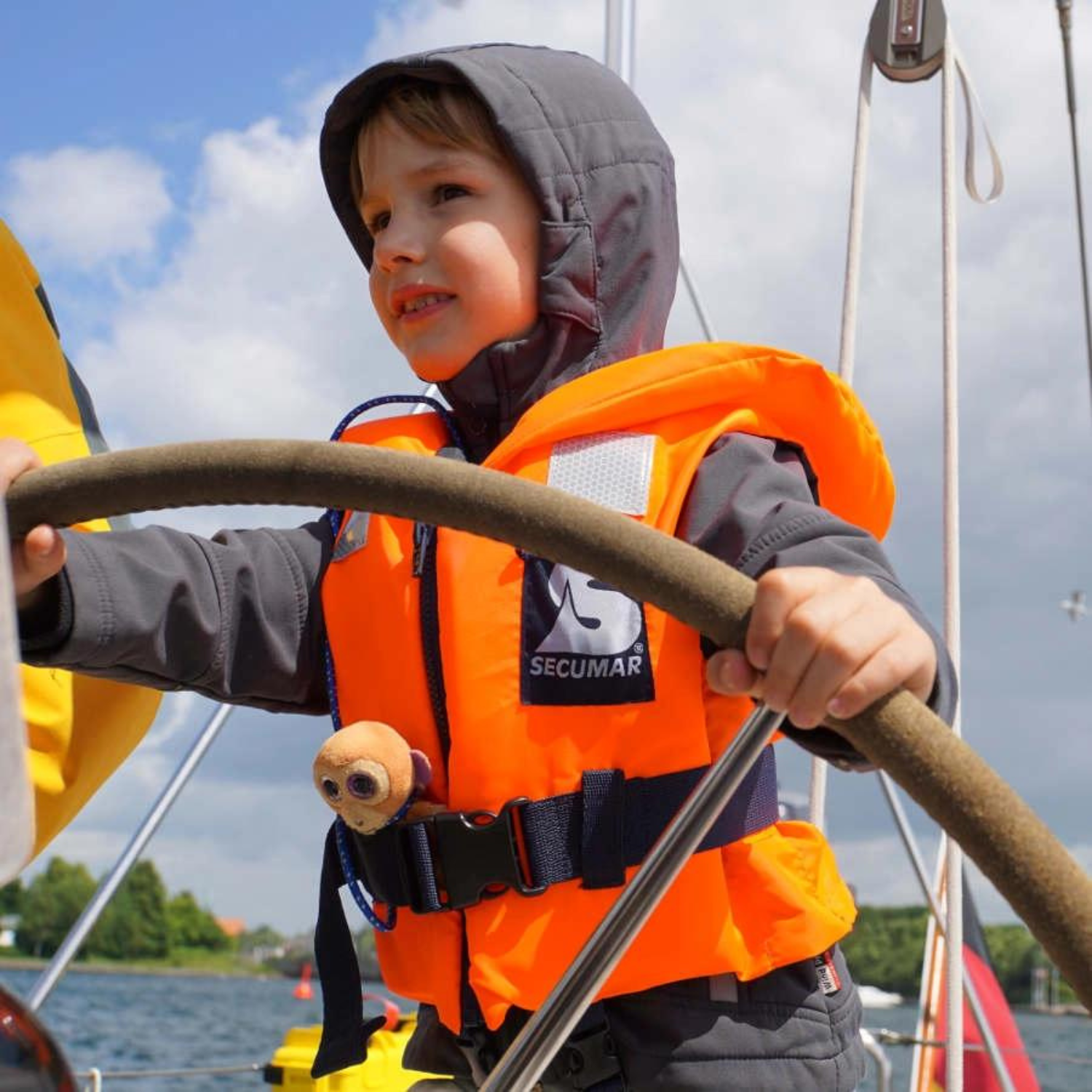 Kind an Steuerrad mit Kinder in Boot mit Secumar Bravo Schwimmweste orangerot