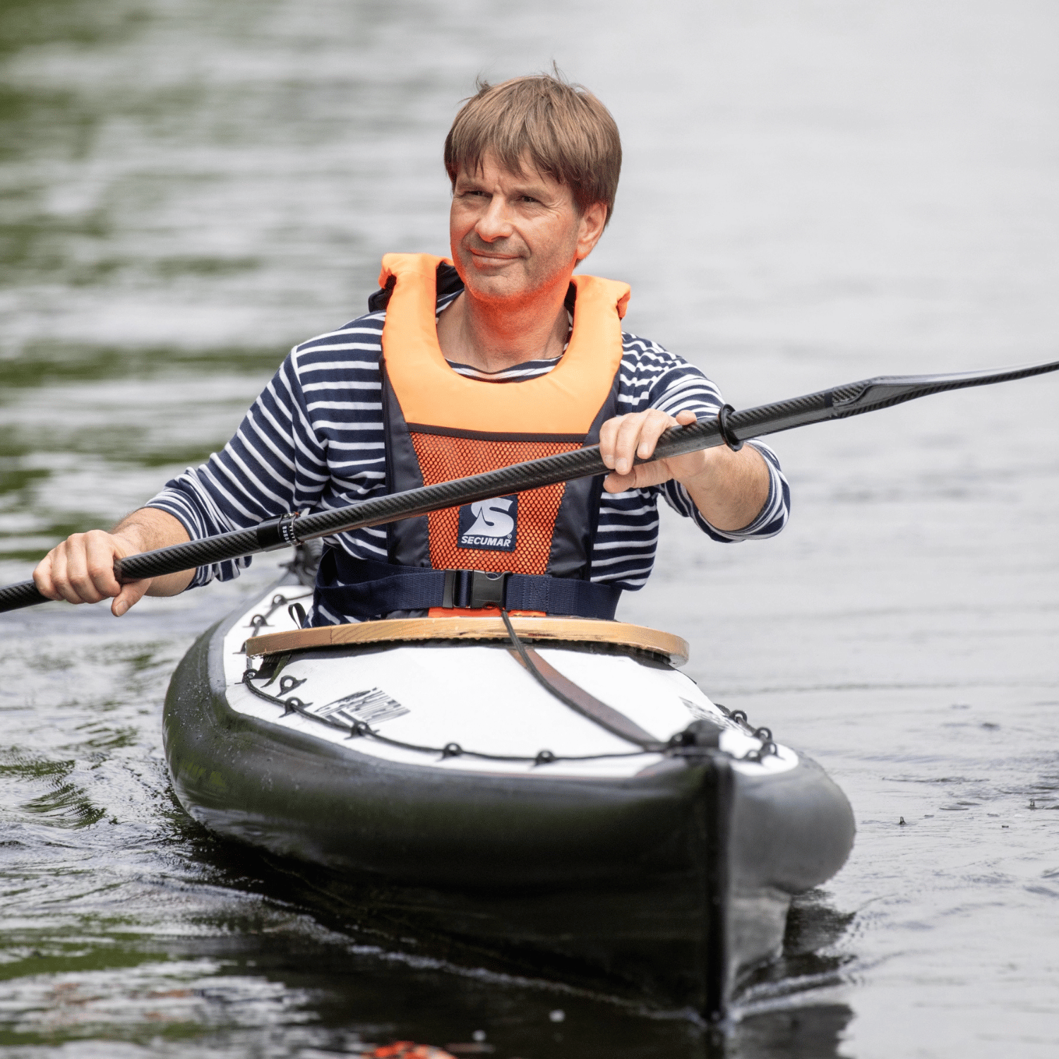 Mann in einem dunkelgrauen Kanu mit Secumar Vivo 50N Feststoffweste orange  und schwarz auf dem Wasser mit einem Doppelpaddel