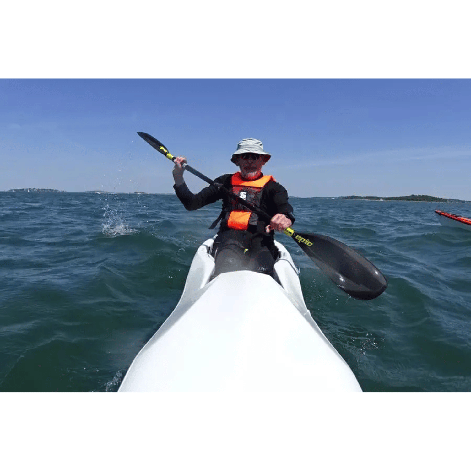 Älterer Mann in einem Boot mit Secumar Vivo 50N Feststoffweste orange und schwarz, der auf dem Wasser mit einem Doppelpaddel paddelt