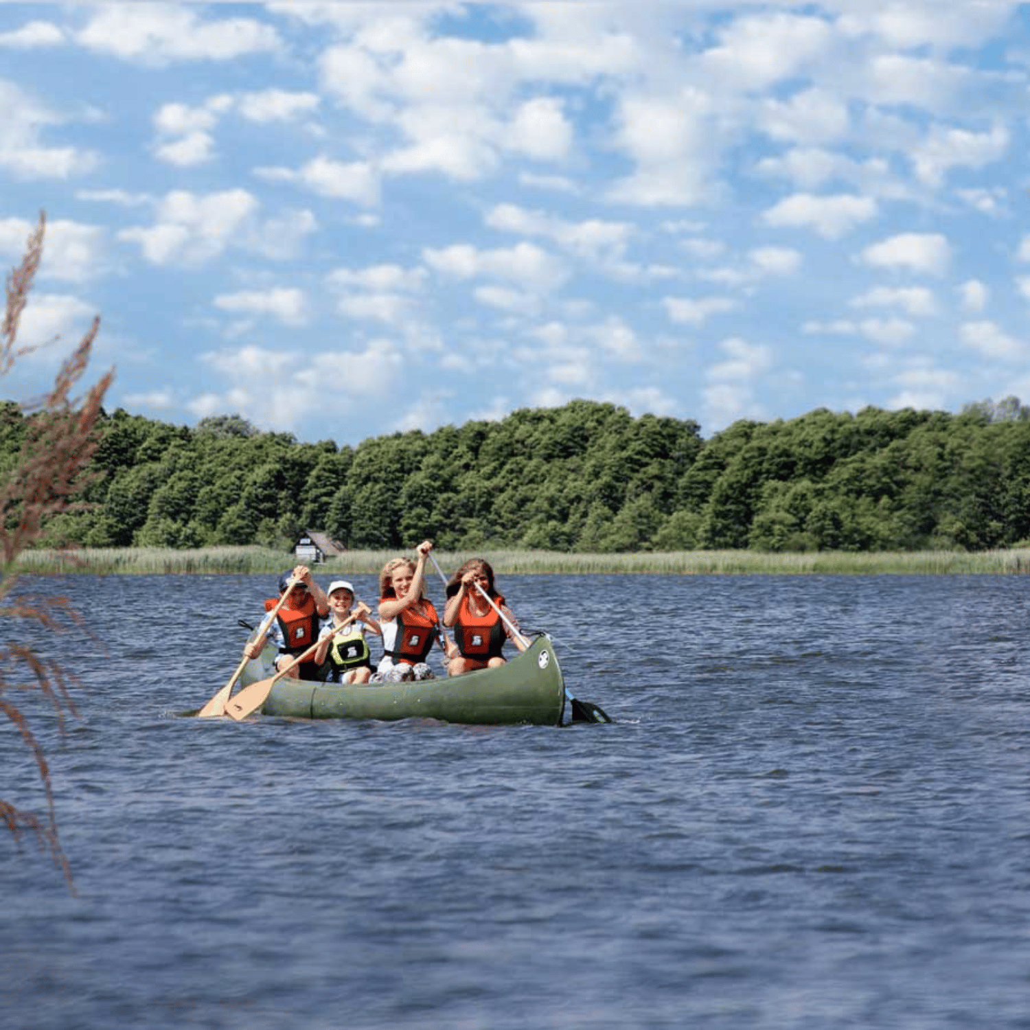 Familie (Eltern und zwei Kinder) in einem dunkelgrünen Kanu mit bie Secumar Vivo 50N orange und schwarz Rettungswesten und Steckpaddeln